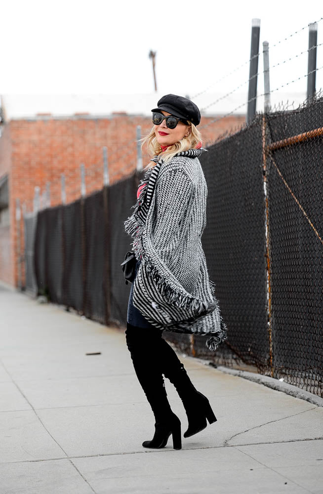 woman wearing a fringe poncho with a red top, black pants and black boots