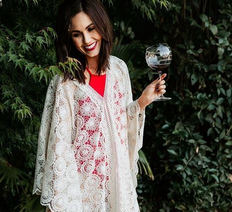 woman wearing a lace cape with red top holding a glass of wine