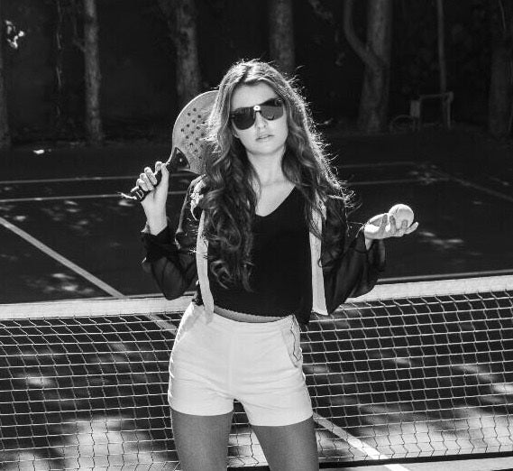 woman wearing a black top, white shorts while carrying a tennis racket