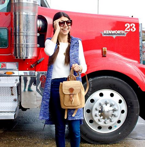 woman wearing a  long vest, white top and denim pants carrying a bag