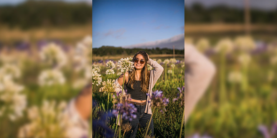 girl wearing sun glasses, standing between flowers and smiling