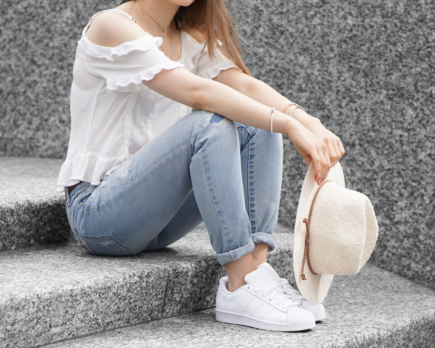 woman sitting on a step wearing a white top, denim pants and white sneakers