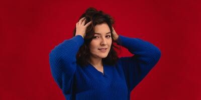 women wearing blue sweater with red background holding her hairs